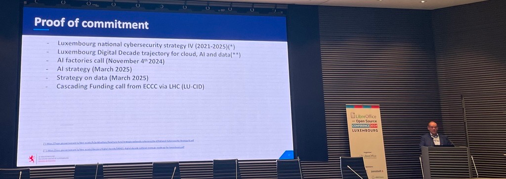 The image shows Franรงois THILL giving a presentation at the Belval Campus of the University of Luxembourg. There is a slide, showing policies and activities showcasing Luxembourg's commitment to cybersecurity.
