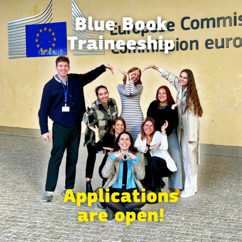Eight young people smile in front of a European Commission building and form a large heart shape together with their arms. The EU flag logo is visible behind them, and overlaid text reads “Blue Book Commission Traineeship” and “Applications are open!”.