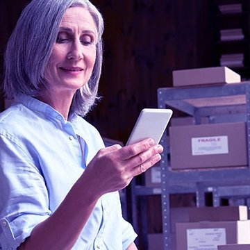 The image of a woman checking a smartphone in a storage with boxes and folders.
